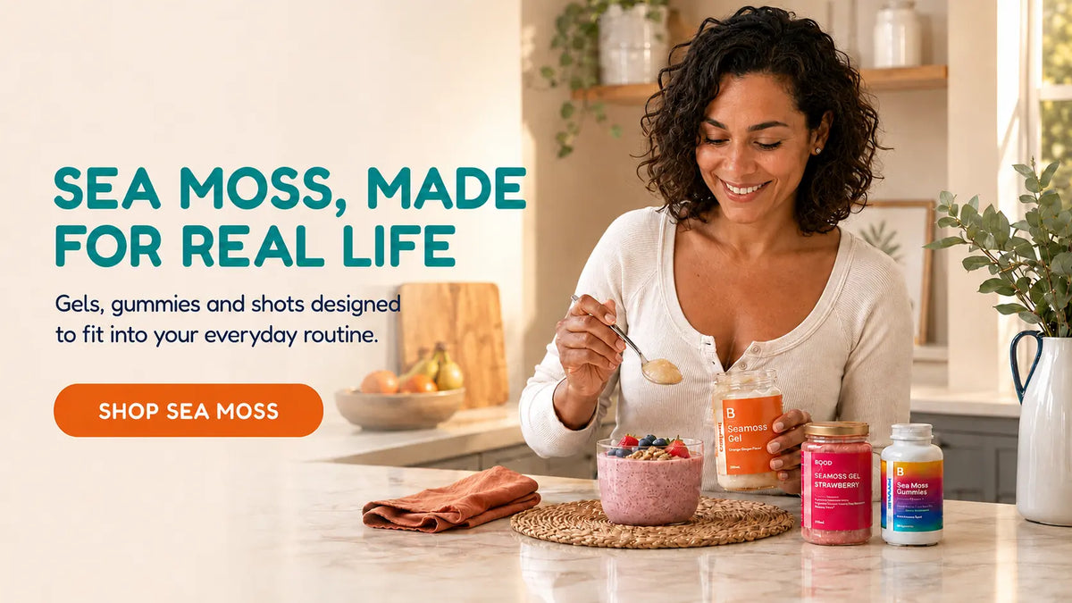 A woman in a bright kitchen smiles while holding a spoon over a jar of sea moss gummies, with several colorful supplement bottles and a bowl of fruit on the counter. Large text on the left reads 'SEA MOSS, MADE FOR REAL LIFE' with an orange 'SHOP SEA MOSS' button.